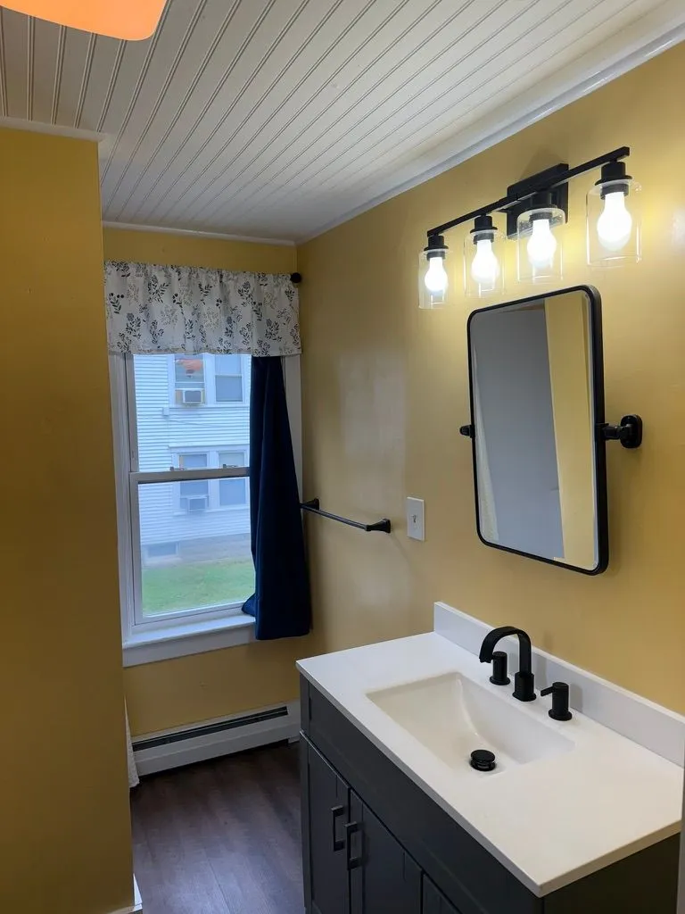 Recently renovated bathroom with a white vanity, black fixtures, yellow walls, and a window at 40 Russell Street